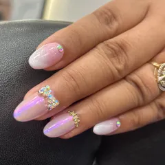 A close-up of the iridescent ombre nail with a hand-placed rhinestone bow. This shows the precision required to create these delicate embellishments that make the design so special.