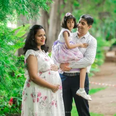 A beautiful family portrait in a park, with the father holding their daughter while the mother cradles her bump. A perfect picture of a growing family.