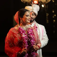 An intimate and candid portrait of the wedding couple. The bride is in the foreground, her expression serene, while the groom stands slightly behind her. The focus on the bride with the groom in soft focus creates a sense of protection and partnership.