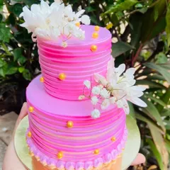 A vibrant pink mini two-tier cake. These smaller tiered cakes are perfect for intimate celebrations, offering an extravagant look on a smaller scale. This one is adorned with fresh white flowers.