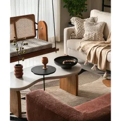 A close-up of the living area, showing the custom reversible cane swing and organic-shaped coffee table. The combination of textures, from the woven pillows to the fluted table base, creates a cozy and inviting setting.