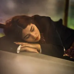 A peaceful and soft-focus portrait of a woman resting her head on her arms. The warm, gentle lighting and her closed eyes evoke a sense of calm and quiet introspection.