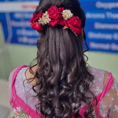 A romantic hairstyle featuring soft curls and a beautiful arrangement of red roses. This half-updo is perfect for a reception or engagement party, adding a touch of classic elegance.