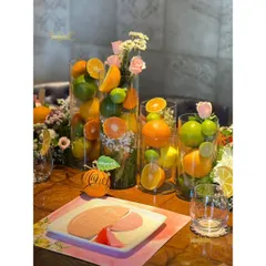 This summer birthday tablescape is bursting with freshness, using tall glass vases filled with whole lemons, limes, and oranges, interspersed with delicate floral bouquets.
