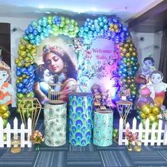 A beautiful Krishna-themed decoration for a naming ceremony, using vibrant blues and greens with peacock feather motifs.