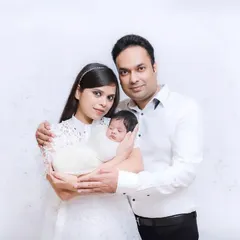 A classic first family portrait with a newborn. The parents look proudly at the camera, holding their new baby, marking the beginning of their journey.