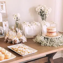 A complete view of a rustic and elegant dessert station. We arranged a naked cake on a bed of baby's breath, along with cookies, cake pops, and matching white gift bags for guests to take home a sweet memory.