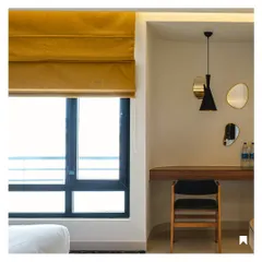 A detail of the study nook in a guest room, featuring a simple wooden desk and organically shaped mirrors. The mustard-yellow roman blinds add a pop of color and warmth.