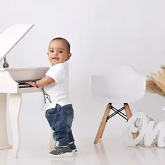 A little boy dressed as a mini-musician, standing and playing at a small white piano in a clean, modern studio setup.