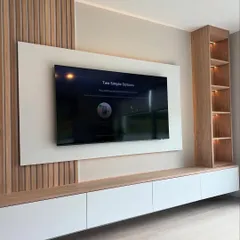 An angled view of a modern entertainment center, showing how the different elements like the wooden paneling, white TV mount, and open shelving come together to create a balanced and functional design.