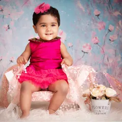 Dressed in a vibrant pink dress against a beautiful floral backdrop, this little girl's smile lights up the entire photo. These sessions are all about capturing the pure joy of being a baby.