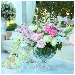 A delicate arrangement of pink and white roses in a crystal compote dish, perfect for a coffee table or lounge area. The addition of fresh jasmine buds in smaller bowls adds a fragrant touch.