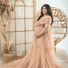 A serene solo portrait of an expecting mother in a beautiful peach gown, seated on a boho-style wicker chair. This shot is all about capturing that quiet, powerful glow of motherhood.