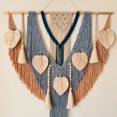 This custom macrame wall hanging was designed with a beautiful color palette of dusty blue, tan, and deep navy. The piece measures 40 inches wide and features multiple knotted patterns, tassels, and leaf details, making it a substantial and eye-catching work of art.