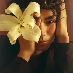 A soft, intimate portrait from a series exploring masculinity and vulnerability. The lily flower held close to the face adds a gentle, poetic element to the image.