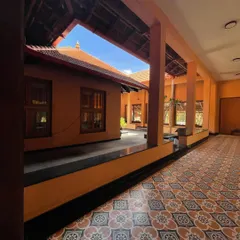 A view along the veranda of the 'SHANTHA-KAMALA' home, where patterned cement floor tiles and earthy orange walls lead the eye towards the central courtyard.