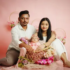 A beautiful family portrait against a soft pink backdrop. The parents cradle their newborn daughter in a flower-adorned basket, creating a sweet and coordinated look. We provide all outfits and props for a stress-free session.