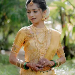 A stunning portrait of the bride in her golden-yellow silk saree. The soft, natural light highlights her traditional jewelry and graceful posture.