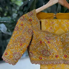 A close-up of the sweetheart neckline and detailed sleeve work on the mustard yellow bridal blouse. The combination of zari, threadwork, and scalloped edging adds layers of texture and elegance.
