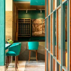 The entrance to the bar area at The Restaurant at Hibiscus. The space is defined by its vibrant teal hues, custom wooden wine racks, and a striking photograph of the Ellora Caves by Amit Pasricha, blending modern design with Indian heritage.