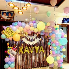A dreamy unicorn party decoration for a tenth birthday, using a soft pastel color palette. This design features an organic balloon garland in pastel pink, yellow, blue, and mint, a shimmering backdrop, and a large unicorn figure. The birthday girl's name "KAVYA" is spelled out in gold foil balloons, adding a personalized touch to this magical setup.
