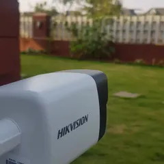 A Hikvision 4MP IP bullet camera installed and focused on the garden and perimeter fence of a property.