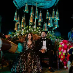 A portrait of Tanmay and Dipika seated on their beautifully decorated stage. The traditional musicians and vibrant decor add to the festive and royal atmosphere of their Sangeet.