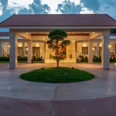 The main portico at dusk, illuminated to create a grand and welcoming entrance. The design uses classical pillars and a circular driveway centered around a bonsai tree, establishing a formal yet serene sense of arrival.