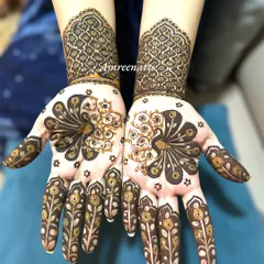 A colorful version of the peacock design, showing the fresh henna paste. The graceful birds are surrounded by delicate floral details on the fingers.