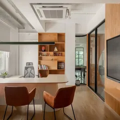 A director's cabin at Hosachiguru, designed with glass walls to maintain the sense of openness and transparency. The room features a custom desk, built-in wooden shelving, and warm, functional lighting.