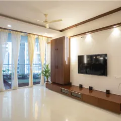 Another angle of the modern living room, showing the comfortable seating arrangement and the view of the balcony. The dark wood accents on the ceiling and TV unit provide a warm contrast to the bright, airy space.