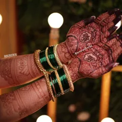 A close-up of the beautiful dark stain, complemented by traditional green bangles. The intricate details of the design are still sharp and clear.