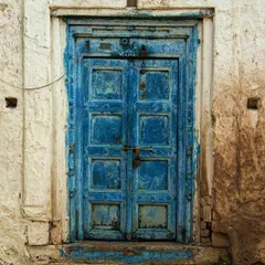 This heavily textured blue door shows years of wear, with layers of paint peeling away to reveal the wood beneath. The rustic locks and bolts add to its vintage, authentic character.