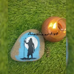 A silhouette of Lord Shiva painted on a smooth river stone, placed next to a candle for a serene evening pooja. This is a simple yet profound piece of spiritual art.