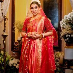 A full-length portrait showcasing the bride in her magnificent red wedding saree. The elegant setting and soft lighting highlight the complete bridal look, from the mukut to the intricate jewelry.