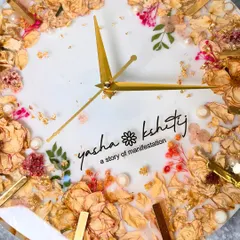 A close-up of a 12-inch wall clock made with a preserved varmala. The mix of dried roses, small pink flowers, and gold accents is just beautiful.