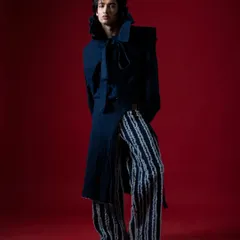This full-length shot showcases the unique silhouette and texture of the designer's creation. The pose is intentionally static to let the clothes do the talking.