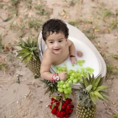 A refreshing milk and fruit bath session. This unique outdoor setup features a baby enjoying a bath with grapes and pineapples, perfect for a summer-themed shoot.