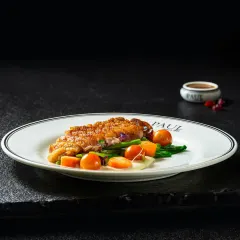 A perfectly cooked crispy skin chicken breast served on a bed of sauteed vegetables, elegantly plated for a fine-dining menu.