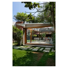 The Komorebi Pavilion seen from the garden, appearing as a light-filled lantern in the landscape. The design uses a minimal steel frame and extensive glazing to dissolve the building's mass, allowing it to merge with the surrounding trees and pathways.