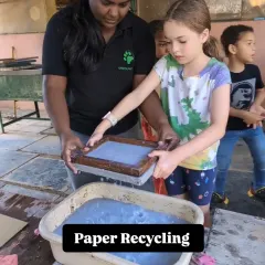 A child learns the process of paper recycling, holding a frame filled with pulp. Our workshops teach sustainable practices in a fun, hands-on way.