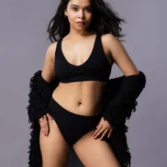 A confident pose in a simple black two-piece lingerie set, paired with a textured black shrug. The grey background keeps the focus entirely on the model.