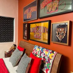 A shot of the headboard, showcasing a collection of framed vintage textiles, including Kapdu and other ethnic embroideries, alongside a colorful patchwork throw.