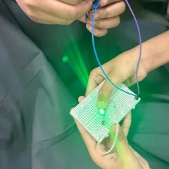 Success! A student holds up a breadboard with a glowing green LED, showing a completed circuit from one of our introductory electronics lessons.
