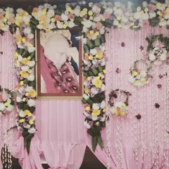 A simple yet beautiful home decoration with a pink backdrop. The portrait of Guru Ji is framed with garlands of mixed flowers, and small floral baskets hang on the sides.