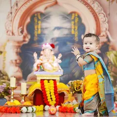 A little devotee waves hello in front of a beautifully decorated Ganesha idol. This full-length shot showcases the traditional attire and the elaborate festive setup.