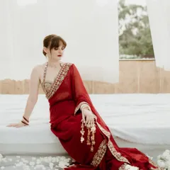 An elegant portrait of the bride in a stunning red saree, seated in a serene, white setting in Jammu. The image is quiet and contemplative, highlighting her grace and beauty.