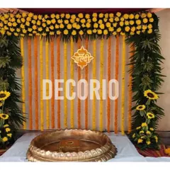 A classic Haldi backdrop combining vertical strings of orange and yellow marigolds. The arch is decorated with yellow flowers and green leaves, with sunflowers adding a fresh touch to the overall design.