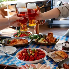 The quintessential "cheers" shot. Hands raising glasses of beer over a table full of food captures the fun, social vibe of a sports bar.