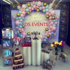 This modern baby shower decor combines a circular balloon arch with fun props like a miniature tricycle, birdcages, and letter blocks. The neon "Baby Shower" sign adds a stylish, contemporary touch.